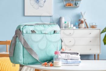 Bottle of milk for baby with clothes and bag on table in room�