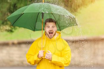 Young man with umbrella wearing raincoat outdoors�