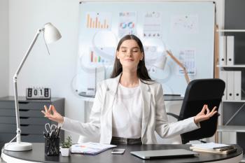 Young businesswoman meditating in office�