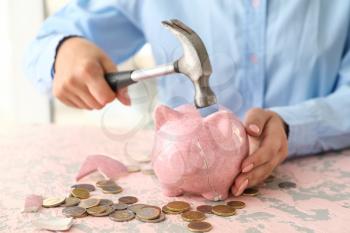 Woman breaking piggy bank at table�
