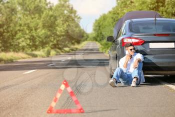 Man calling his insurance near broken car on road�