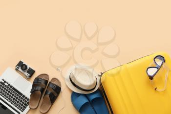 Suitcase with beach accessories and laptop on color background�