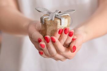 Woman with beautiful manicure holding gift, closeup�