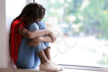 Sad African-American girl sitting on windowsill. Stop racism�