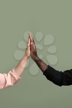 Hands of Caucasian woman and African-American man giving high-five to each other on color background. Racism concept�
