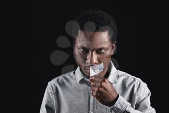 Sad African-American man removing tape from mouth on dark background. Stop racism�