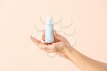 Female hands and travel bottle with body care cosmetics on light background�