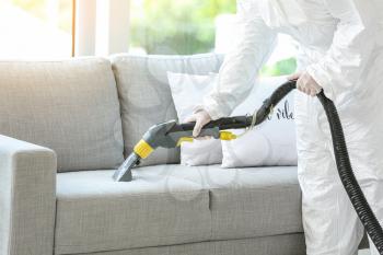 Worker in biohazard costume removing dirt from sofa in house�