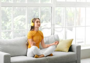 Young woman listening to music while meditating at home�