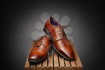 Pair of leather male shoes on wooden box against dark background�