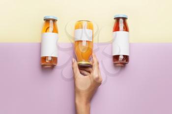 Female hand with bottles of juices on color background�