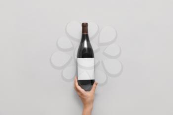 Female hand and bottle of wine with blank label on light  background�
