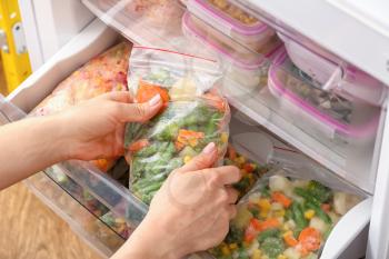 Woman putting plastic bag with frozen vegetables into refrigerator�