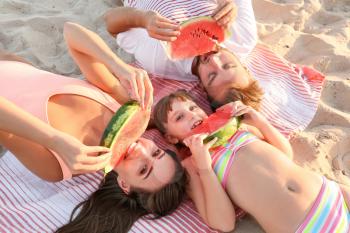Happy family eating watermelon on sea beach�