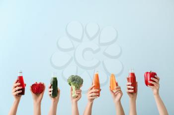 Many hands with bottles of vegetable juices on color background�