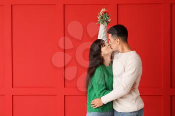 Young couple kissing under mistletoe branch on color background�
