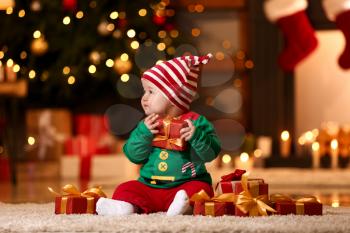 Cute little baby in elf's costume and with gifts at home on Christmas eve�