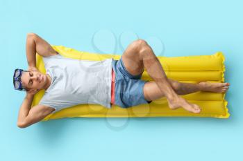 Young man lying on inflatable mattress against color background�