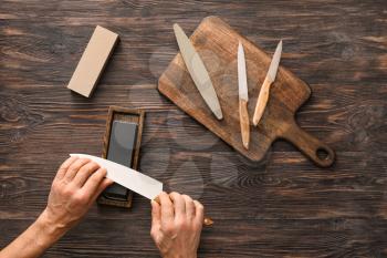Man sharpening knife on wooden background�