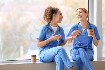 Female doctors drinking coffee while sitting on window sill in clinic�