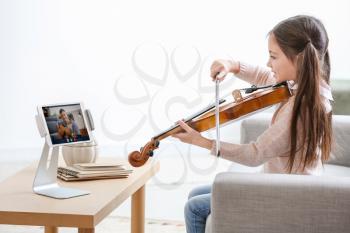 Little girl taking music lessons online at home�