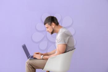 Man with bad posture using laptop while sitting on chair against color background�