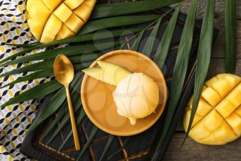 Plate with tasty mango ice cream and palm leaf on wooden background�