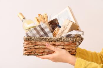 Woman holding gift basket with products on light background�