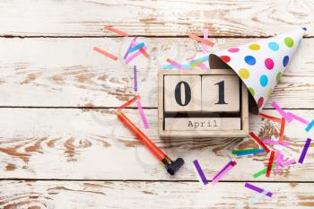 Party decor and calendar with date of April Fools Day on white wooden background�