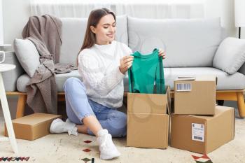Young woman opening parcel with new clothes at home�