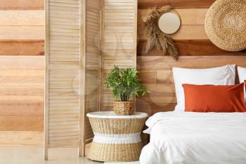 Houseplant on bedside table and folding screen near wooden wall in bedroom�
