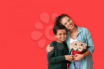 African-American boy and his mother with flowers on color background�