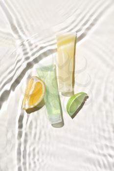 Tubes of cosmetic products and citrus fruits in water on white background�