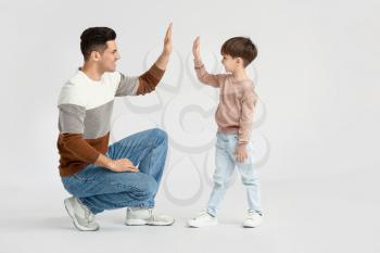 Happy father and his little son giving each other high-five on light background�
