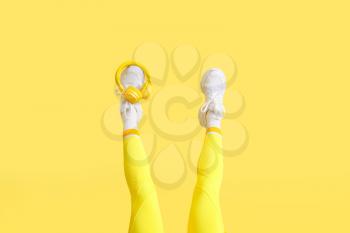 Legs of stylish young woman with headphones on yellow background�