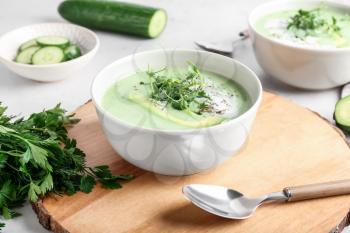 Bowls with green gazpacho and ingredients on light background�