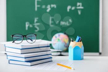 Stack of books and answer sheet forms with eyeglasses on table in classroom�