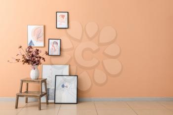 Vase with blossoming branches on table and pictures near color wall�