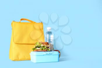 Lunch box bag, bottle of water and sandwich on color background�