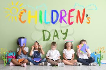Little children with copybooks sitting on floor near color wall. International Children's Day celebration�