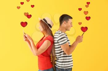 Young couple with mobile phones on yellow background. Online dating�