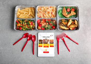 Tablet computer with open page of food delivery site on screen and takeout meals on grey table�