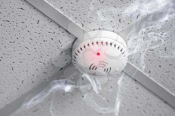 Modern smoke detector in action on ceiling indoors�