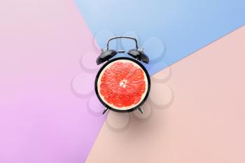 Ripe grapefruit in alarm clock on color background�
