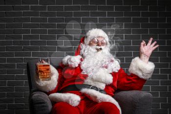 Funny drunk Santa Claus showing OK while sitting in armchair against brick background�