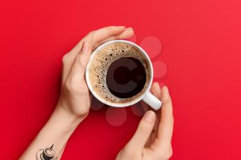 Female hands with cup of hot coffee on red background�