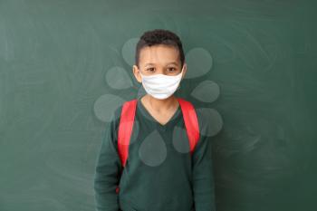Cute African-American schoolboy wearing protective mask in classroom. Concept of epidemic�
