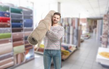 Young man with rolled carpet in modern shop�