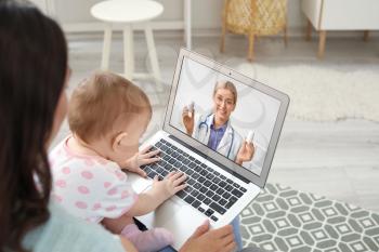 Young woman with her baby getting online consultation at home�