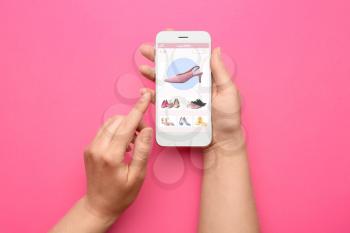 Female hands holding mobile phone with open page of online shoe store on screen against color background�